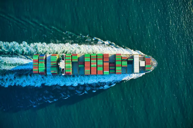Aerial view of a loaded container ship cutting a white wake through open sea